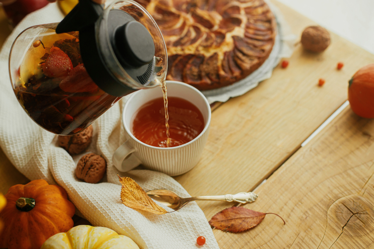 Stoomende mok met appeltaartthee – gevuld met kleine appelstukjes en amandel­vlokken; een schijfje sinaasappel en een kaneelstokje hangen losjes tegen de rand.